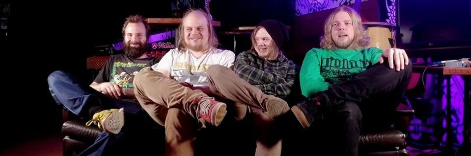 FUCK-USHIM-bändin neljä jäsentä istuvat rinnakkain pienellä sohvalla musiikkiklubiympäristössä.