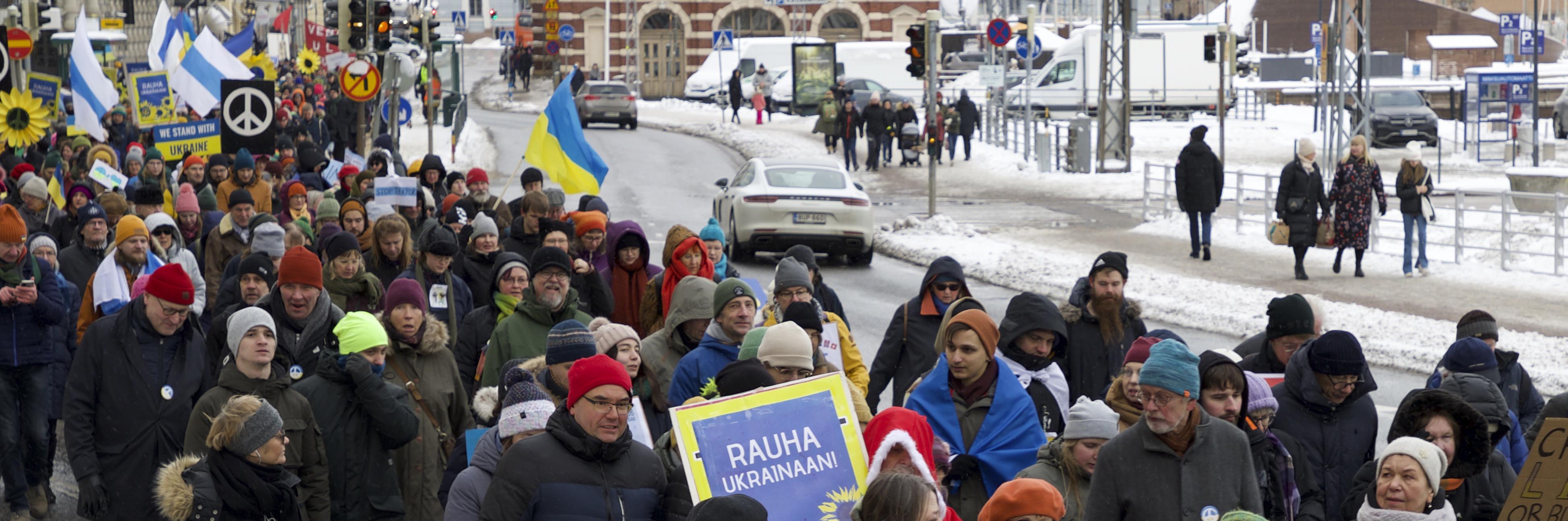 People marching in the street with banners that read "Rauha Ukrainaan!"