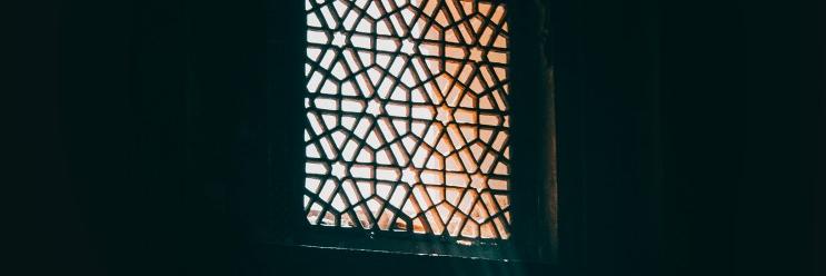 Islamilaisilla ornamenteilla koristeltu ikkuna, jonka läpi siilautuu auringon valoa.