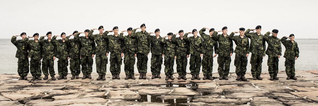 Valokuva Kesälomana sotilasleiri -sarjasta. Joukko teini-ikäisiä seisoo kalliolla rivissä maastoasuissa ja tekee kameralle sotilastervehdyksen.