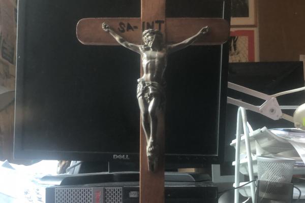 A sculpture of Jesus crucified is visible, and a monitor is visible behind it. The Jesus sculpture has ‘SAINT’ written on it.