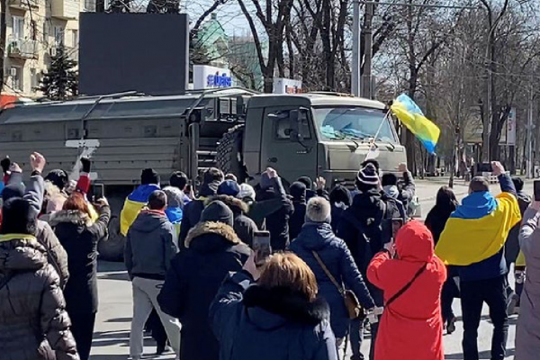 people standing in the street with holding a Ukrainian flag block the path of a Russian tank 