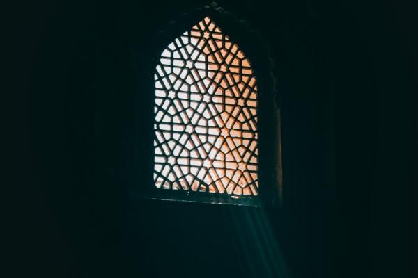 Islamilaisilla ornamenteilla koristeltu ikkuna, jonka läpi siilautuu auringon valoa.